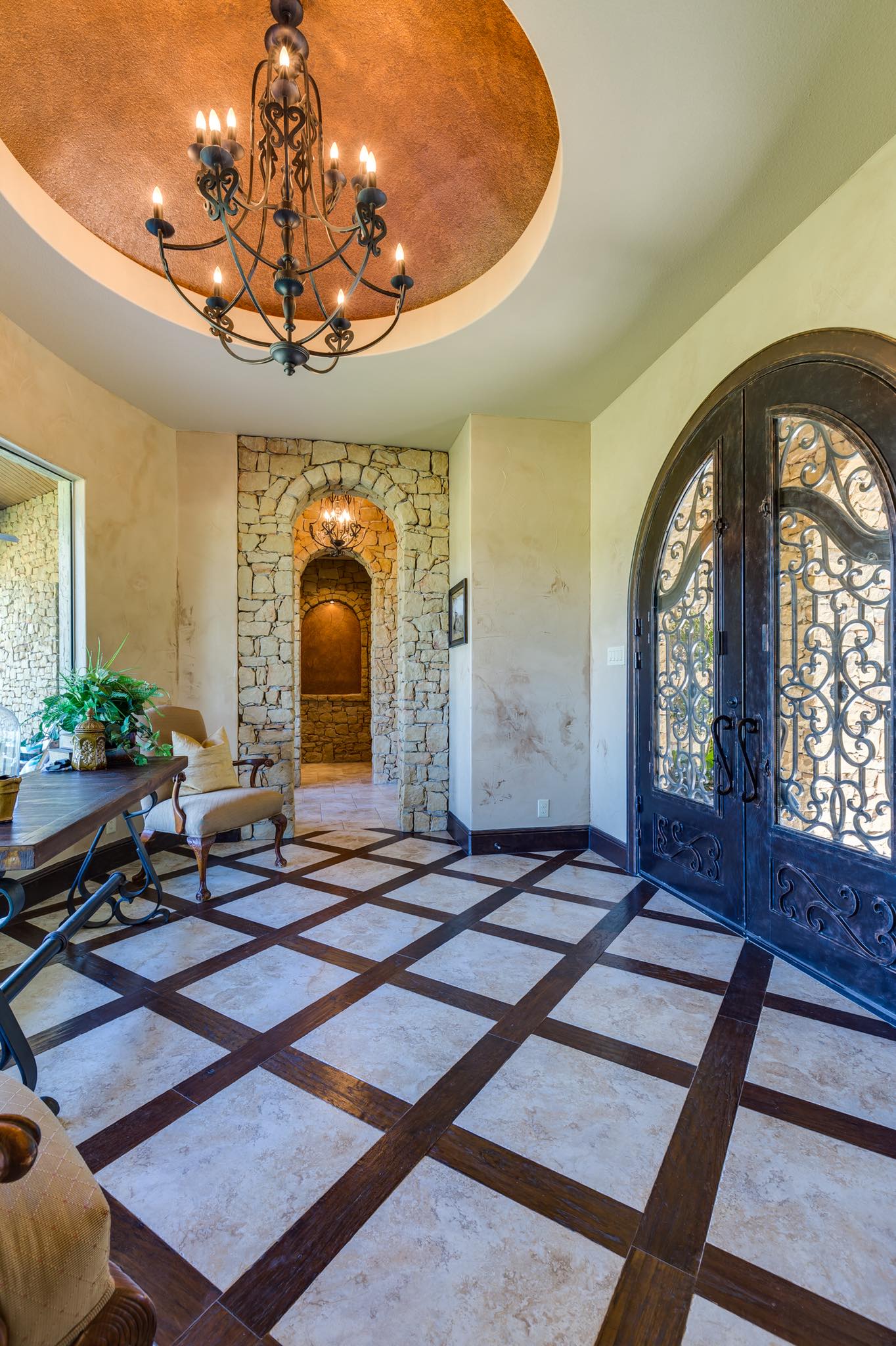 Grand rotunda entryway with wrought iron doors, stone archway, and chandelier